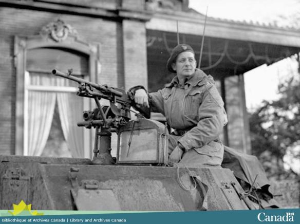Photo noir et blanc montrant un homme assis sur la tourelle d’un char d’assaut appuyé sur la mitrailleuse et regardant vers la gauche.