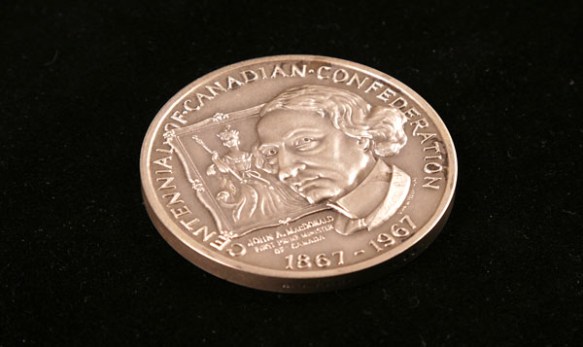 Photographie en couleur montrant une pièce de monnaie avec l’image de John A. Macdonald et un portrait d’une reine dans l’arrière-plan.