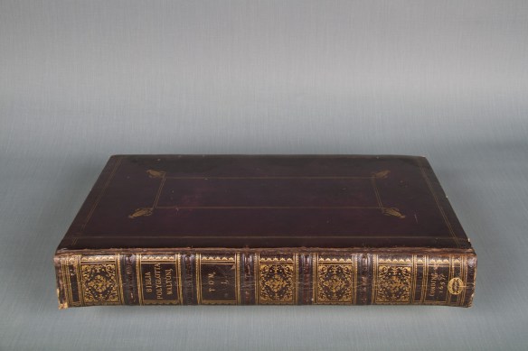 Photographie couleur d’un livre richement décoré à la feuille d’or, portant sur son dos l’inscription Bibla Polyglotta Walton.