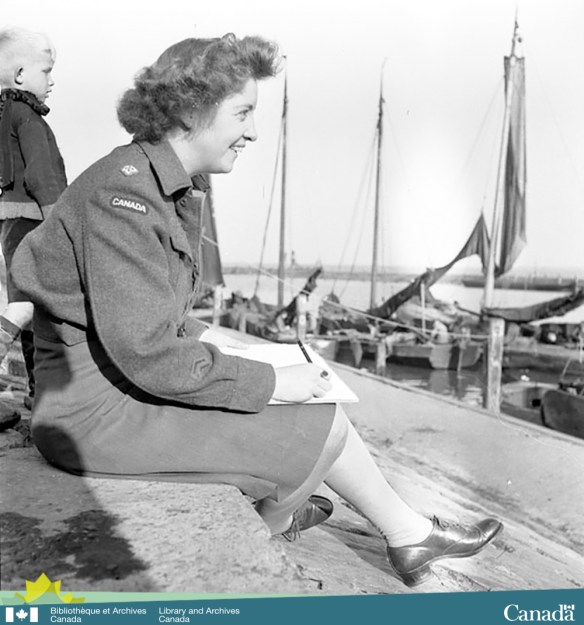 Photographie en noir et blanc prise de côté montrant une femme en uniforme souriante assise sur un quai avec un tableau à dessin et un crayon dans la main. En arrière-plan, on voit un jeune enfant blond et des voiliers à quai.