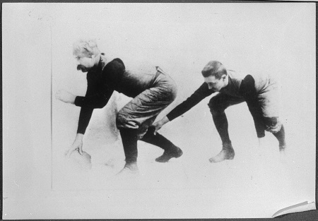 Une photographie en noir et blanc de deux joueurs de football rugby accroupis, l'homme sur la gauche tient le ballon et attend de le lancer à l'autre homme derrière lui.