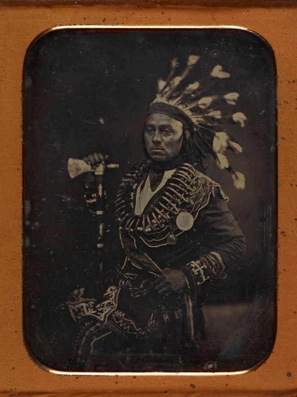 Un portrait de Maungwudaus, vêtu d’une tenue cérémoniale comprenant une coiffe de plume et ses deux médailles. 