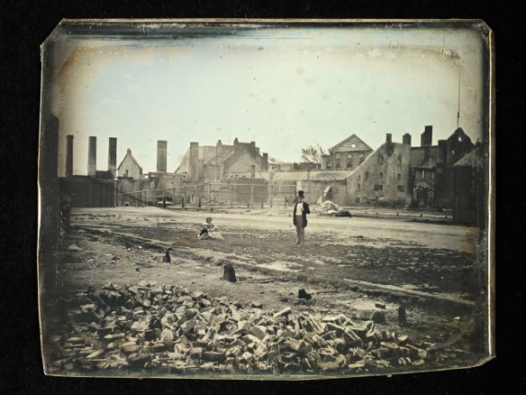 La photo d’un homme debout et d’une femme assise, parmi les ruines de la brasserie. 