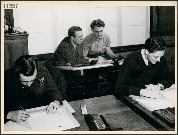 Photo en noir et blanc montrant des étudiants dans une salle de classe d’une école technique et un enseignant travaillant avec un étudiant.