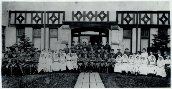 Photographie en noir et blanc d’hommes en uniforme et d’infirmières assis dans un vestibule somptueux de style élisabéthain.