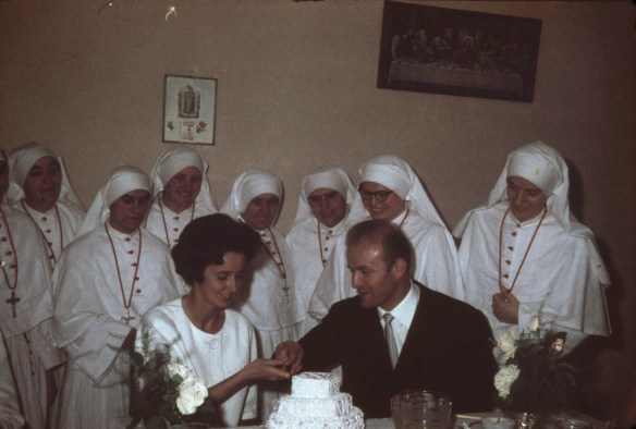 Une photographie en couleur montrant un groupe d’infirmières entourant deux personnes qui s’apprêtent à couper un gâteau de mariage.
