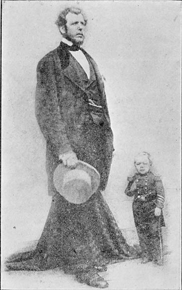 Photographie en noir et blanc de deux hommes debout : l’un est très grand et l’autre est très petit.
