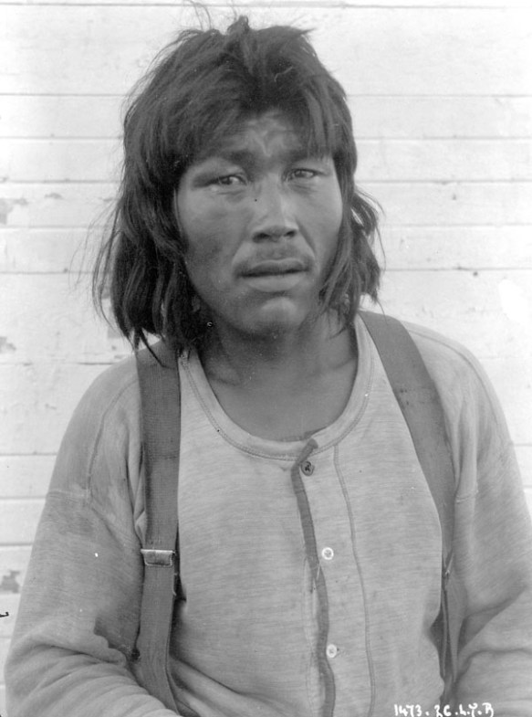 Photographie en noir et blanc d’un homme inuit vêtu d’une chemise et de bretelles et regardant directement le photographe. 