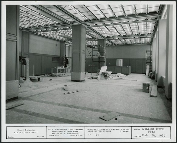 Photographie en noir et blanc d’une grande salle avec un échafaudage et des matériaux de construction. 