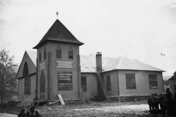 Une photographie en noir et blanc montrant une église placardée sur un terrain jonché de matériaux de construction