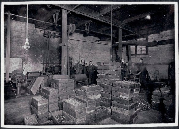 Photographie noir et blanc montrant des employés à l’intérieur d’une usine en train d’empaqueter des produits. 