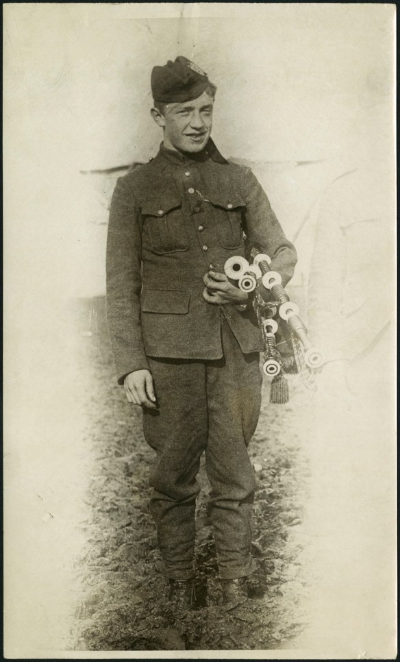 Photographie en noir et blanc d’un jeune homme vêtu d’un uniforme militaire et tenant sa cornemuse.