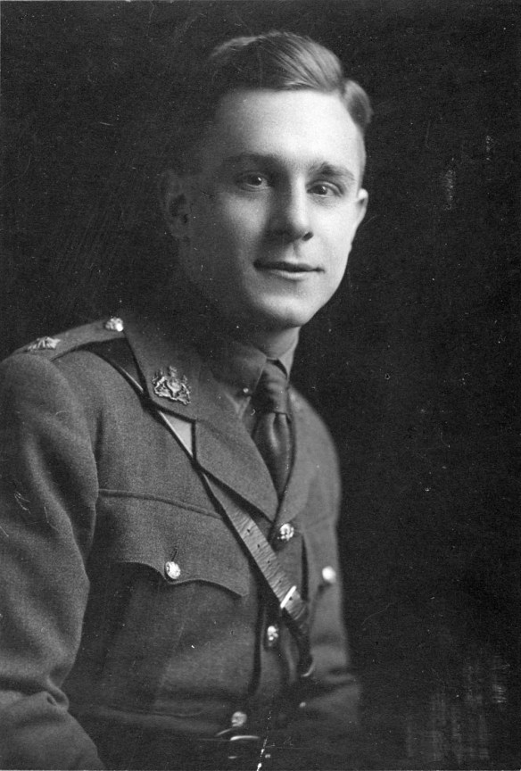 Un portrait en noir et blanc montrant un jeune homme en uniforme. Il est assis, face à l’appareil photo et esquisse un léger sourire.