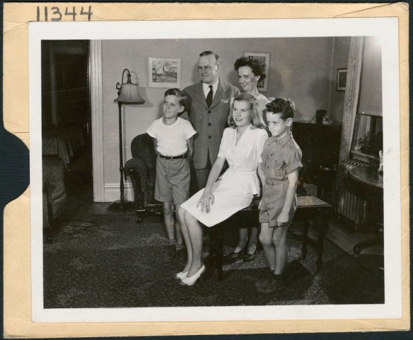 Photographie noir et blanc d’une famille comprenant une femme, un homme et trois enfants dans un salon.