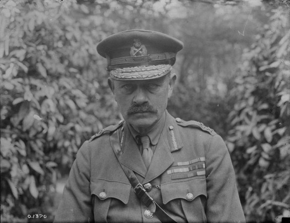 Une photo noir et blanc d’un homme moustachu en uniforme portant une casquette d’officier ainsi que la ceinture Sam Browne. Son blouson est couvert de médailles et de décorations militaires. Il regarde directement le photographe avec un regard impassible.