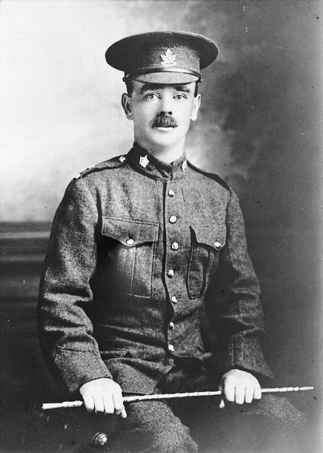 Photographie en noir et blanc d’un soldat assis tenant un bâton et regardant directement le photographe.