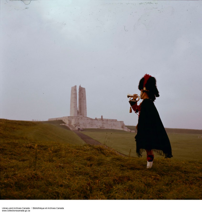 Photographie couleur d’un clairon vêtu d’un uniforme écossais, posant devant le monument sur la crête de Vimy.