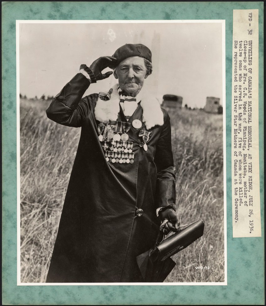 Photographie en noir et blanc d’une femme faisant le salut militaire. Elle est vêtue d’un béret et d’un manteau sur lequel sont épinglées de nombreuses médailles.