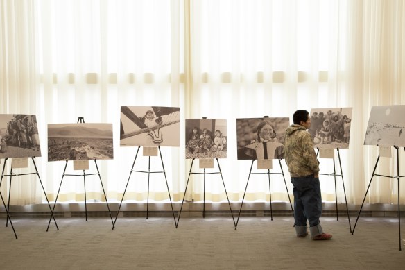 Photographie en couleurs d’un jeune Inuit regardant plusieurs grandes photographies sur des chevalets.