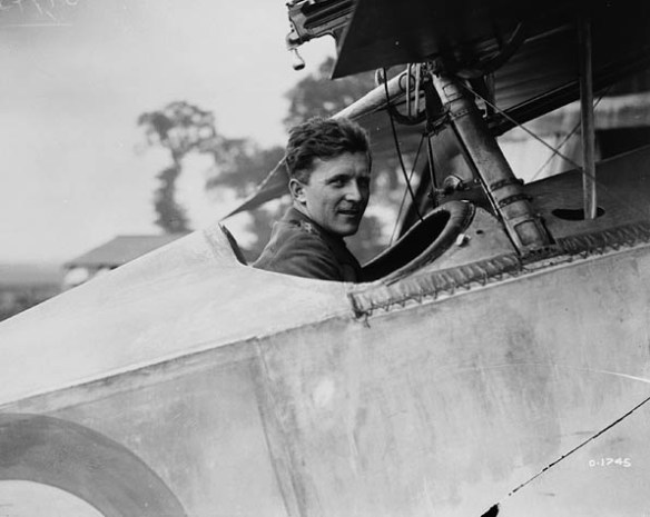 Photographie en noir et blanc d’un homme assis dans le poste de pilotage ouvert d’un avion et regardant le viseur.