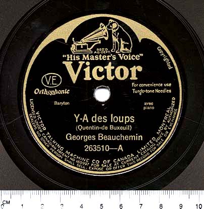 Photographie en couleur d’une étiquette circulaire noire au centre d’un disque 78 tours. En lettres dorées, on peut lire : « His Master’s Voice. Victor. Y-A des loups (Quentin-de Bexeuil). Georges Beauchemin. 263510-A ».