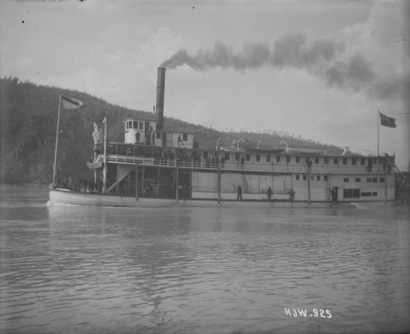 Une photo noir et blanc d’un bateau à vapeur avec des passagers. Des gens sont sur l’avant du bateau tandis que d’autres sont debout sur la passerelle du deuxième étage.