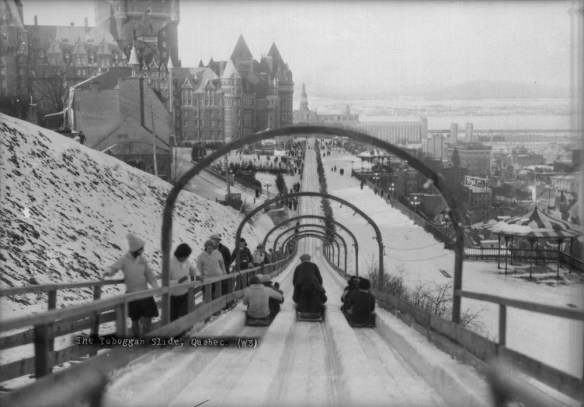 Photographie en noir et blanc de gens sur des toboggans glissant la piste tandis que d’autres personnes montent la cote.