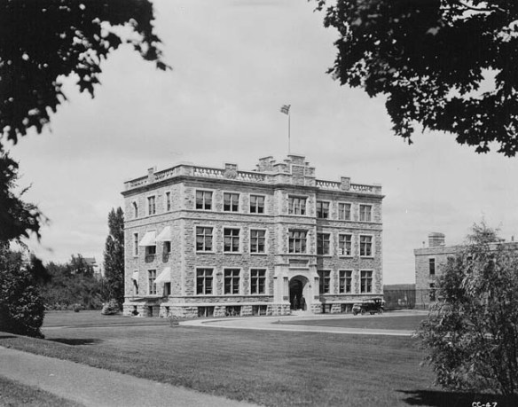 Une photo en noir et blanc d’un edifice de trois étages en pierre situé dans un espace avec une grande pelouse