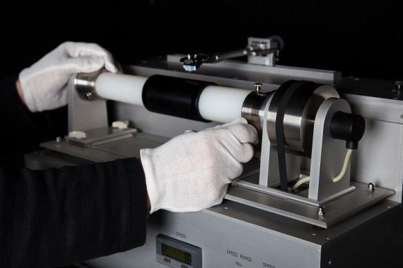 Une photographie couleur montrant un lecteur de cylindre avec un cylindre Blue Amberol passé sur un tube horizontal, ainsi qu’une aiguille oscillant au-dessus du cylindre.