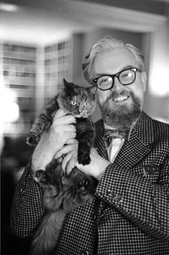 Une photo noir et blanc d’un homme souriant qui tient un chat sur son épaule.