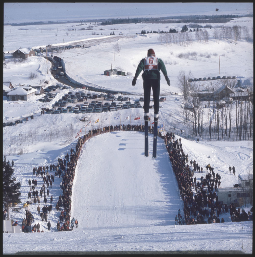 Une photo en couleur d’un sauteur voltigeant au-dessus d’une foule de spectateurs.