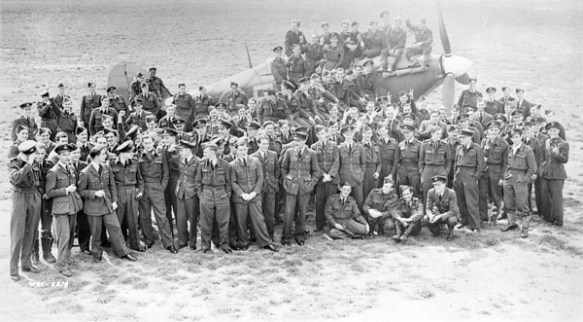 Photo noir et blanc d’un groupe d’officiers de la force aérienne posant devant un avion de chasse Hawker Hurricane.