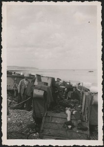 Photo noir et blanc de civils s’occupant des dépouilles de soldats morts dans une péniche de débarquement échouée sur la plage.