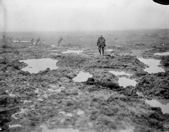 Photographie en noir et blanc d’un soldat marchant dans un champ couvert de boue et de flaques d’eau.