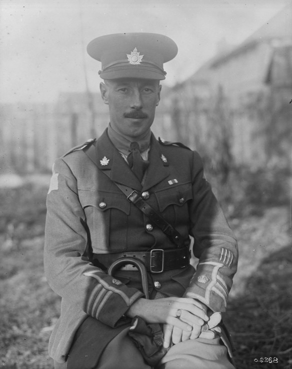 Photographie noir et blanc d’un officier assis portant une casquette et une ceinture Sam Browne (large ceinture en cuir entourant la taille à laquelle est attachée une bande plus étroite placée en diagonale et qui passe sur l’épaule droite); il y a des galons sur les manches de sa veste. 