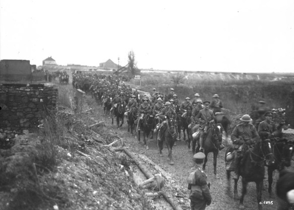 Photographie en noir et blanc de soldats à cheval traversant un village.