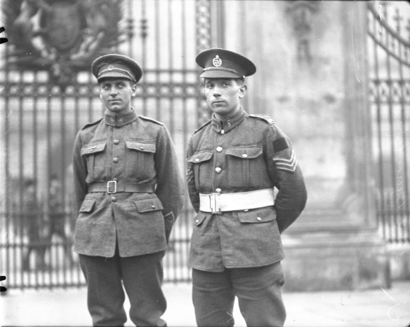 Photo noir et blanc de deux soldats debout devant une grille en fer forgé ouvragé. 