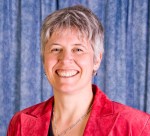 Photo en couleur d'une femme portant un veston rouge devant un rideau bleu et arborant un grand sourire.