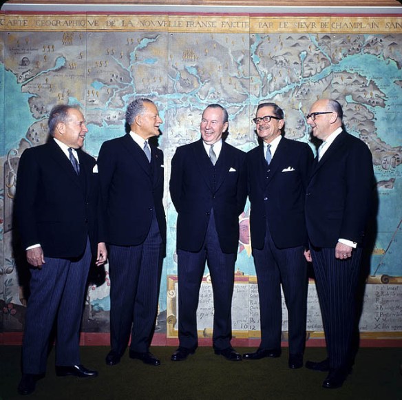 Photographie en couleurs d’un groupe d’hommes debout devant l’agrandissement d’une carte de la Nouvelle-France.