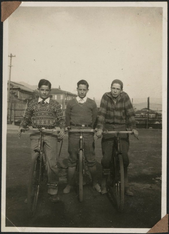 Photographie en noir et blanc montrant trois garçons sur des vélos.