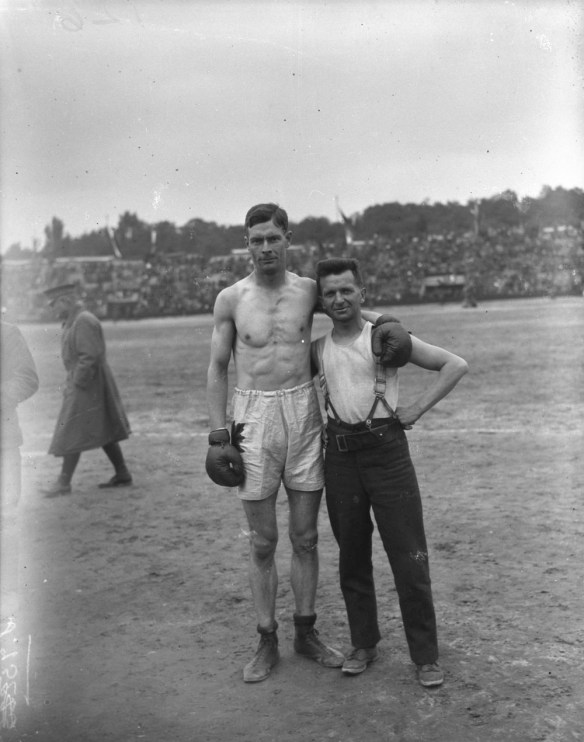 Photographie en noir et blanc du boxeur de la catégorie des poids moyens Edwin A. Harris (Canada), portant le short et les gants. Un autre soldat se tient debout à ses côtés.