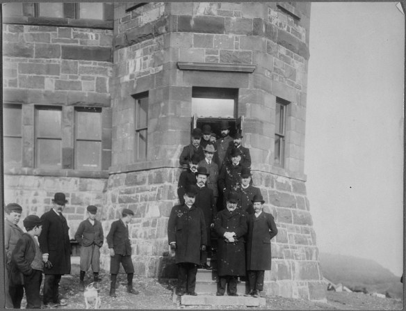Photographie en noir et blanc de Guglielmo Marconi posant sur les marches d’un bâtiment avec 12 membres de l’administration de Terre-Neuve, colline Signal, St. John's.