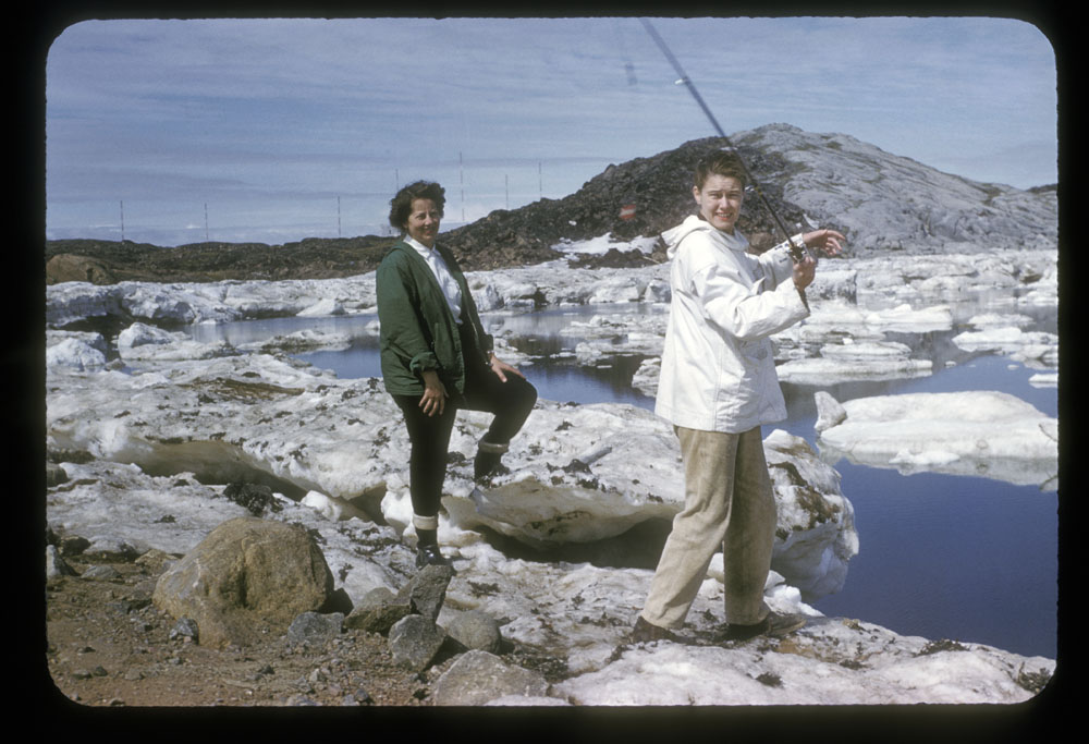 Photographie couleur de deux femmes en train de pêcher sur les rives d’un plan d’eau. Elles sont debout sur des roches, et des plaques de glace flottent sur l’eau.