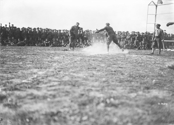Une photographie noir et blanc d’un joueur glissant vers le marbre. Le receveur se tient derrière le marbre alors que l’arbitre rend sa décision. Une foule composée de soldats les encourage.