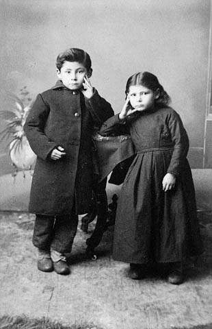 Photo noir et blanc de deux enfants appuyés contre un guéridon, une main sur la joue.