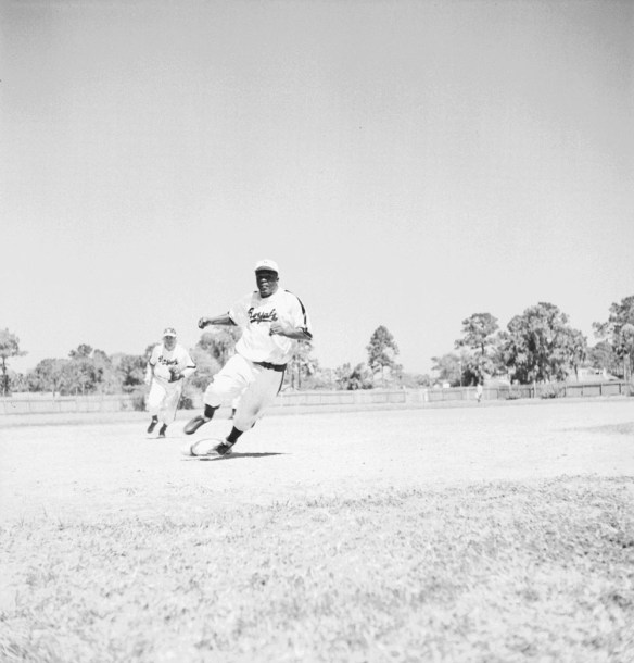 Une photographie noir et blanc d’un joueur de baseball courant entre les buts alors qu’un joueur de l’équipe adverse essaie de le rattraper.