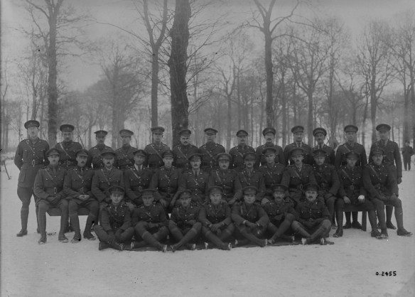 Photographie en noir et blanc d’un groupe de soldats debout et assis devant des arbres en hiver. 