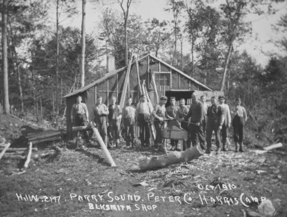 Photographie en noir et blanc de treize hommes prenant la pose devant la forge. 
