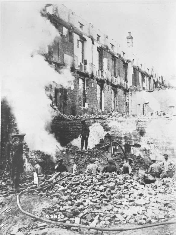 Photo noir et blanc de soldats en uniforme travaillant au milieu des décombres d’un grand bâtiment de briques lourdement endommagé par un bombardement.