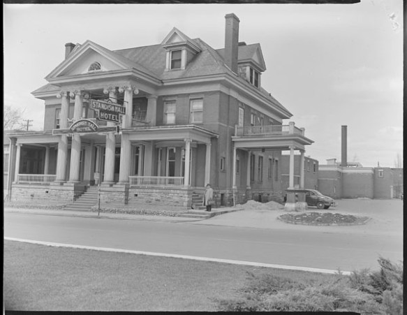 Photo noir et blanc d’un gros bâtiment avec une large terrasse et une pancarte sur laquelle est inscrite « Standish Hall Hotel ».